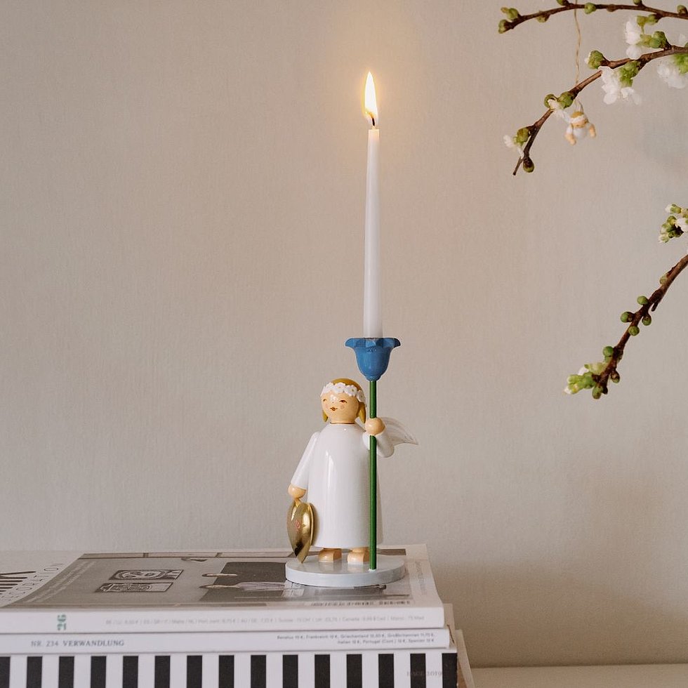 Großer Margeritenengel mit goldenem Herz und blauer Kerzentülle auf einem Stapel Bücher neben einem Strauß mit Zweigen