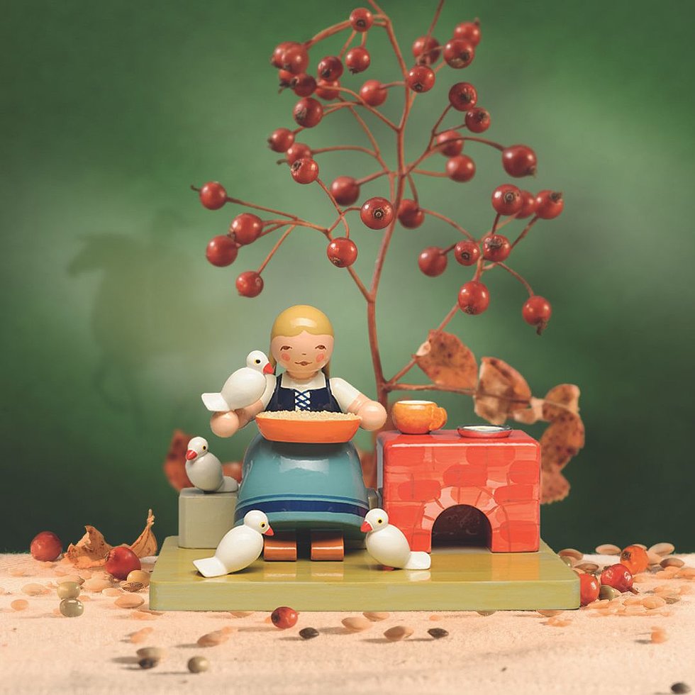 Figur, die Aschenbrödel nachempfunden ist, wie sie am Kachelofen Linsen sortiert. 