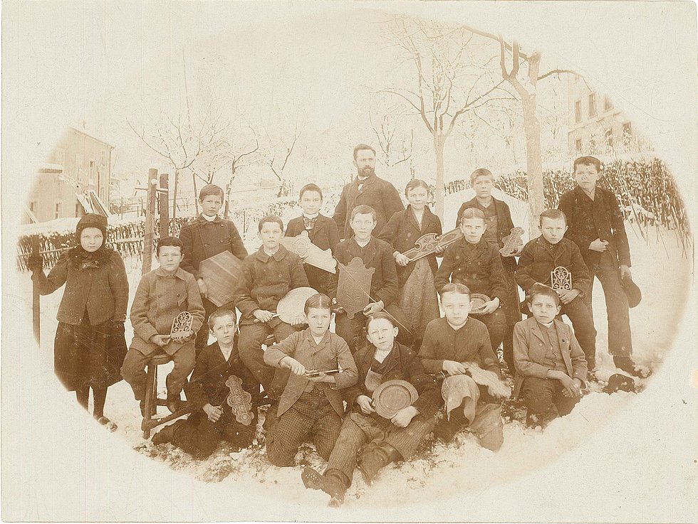 [Translate to Niederländisch:] Historische Aufnahme. Klassenfoto aus der Gewerbeschule. Grete Wendt als einziges Mädchen in der Klasse. Aufnahme im Winter, die Kinder sind in Mäntel und Mützen gekleidet. Es liegt Schnee.